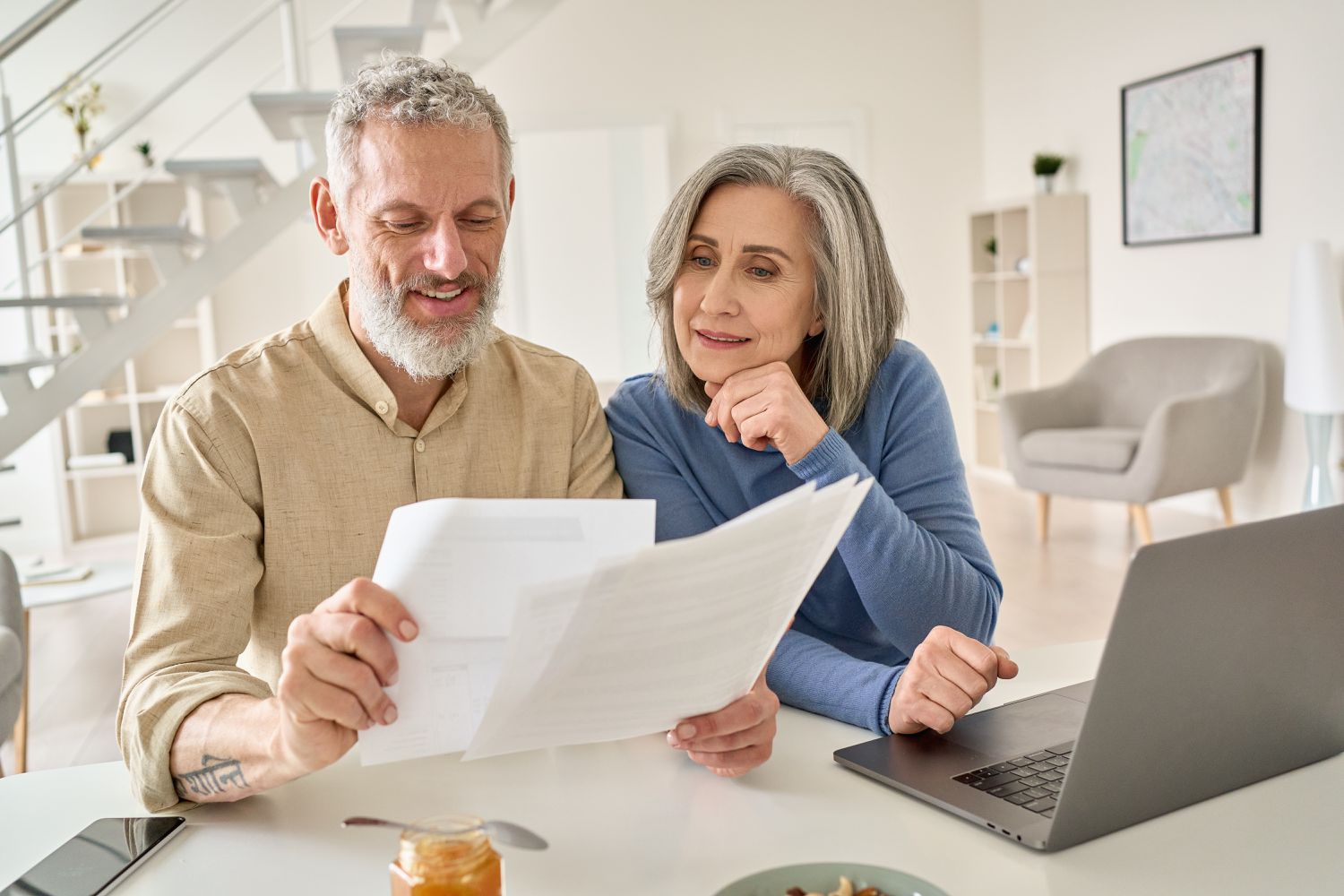 Older couple looks over documents while sitting in front of laptop computer in their home