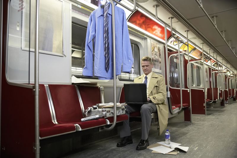 A man in empty subway train, using laptop.