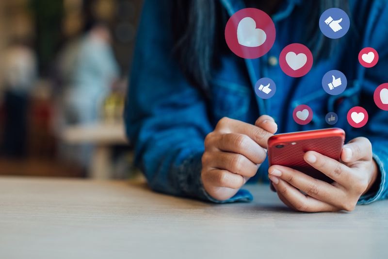 midsection of woman using a smartphone with facebook hearts and likes graphics in the air