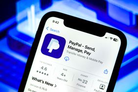 The App Store page for PayPal is seen on a cell phone screen in front of a blue background.