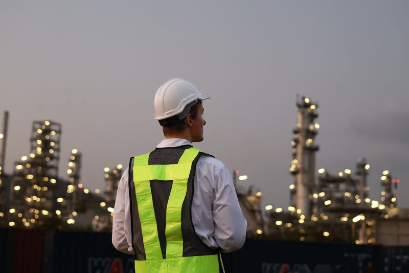 A chemical engineer working the night shift at a petroleum oil refinery stands on a rooftop to observe the lights of the refinery.