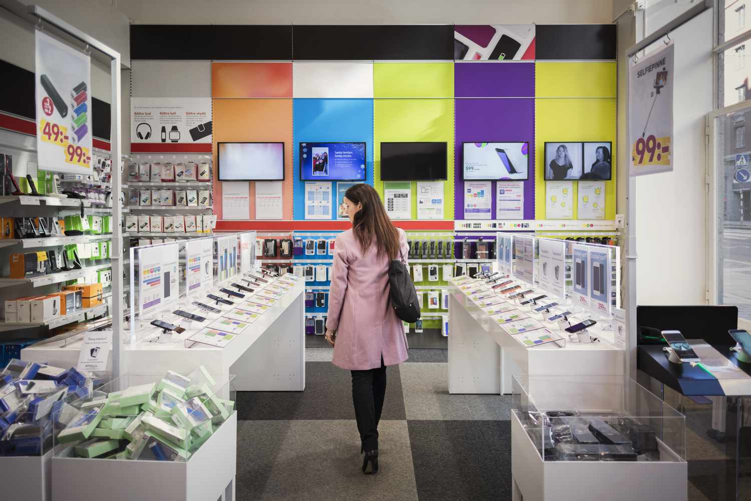 A store shopper walking between isles in an electronics store filled with a wide variety of products.