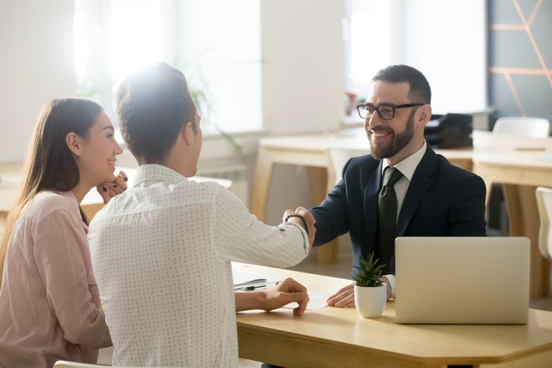 Smiling financial advisor shaking hands with a couple after helping them out with decisions about insurance policies and bank investments.