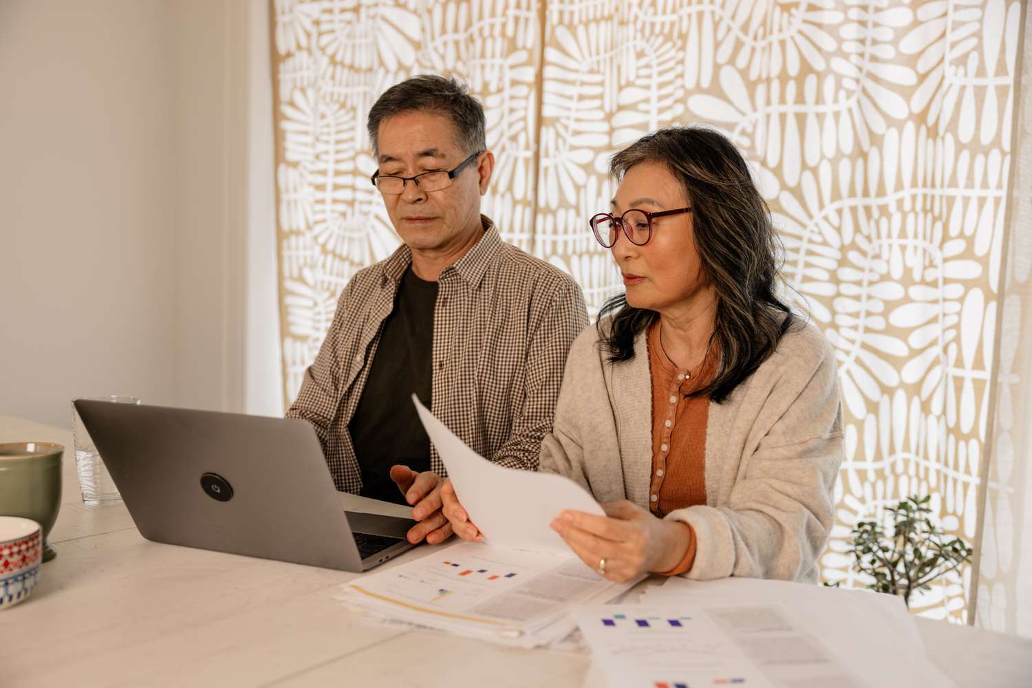 Older couple sitting in their kitchen and looking at mortgage documents and a laptop