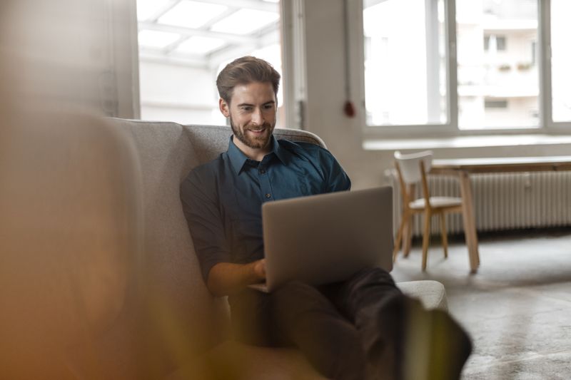 Man in his late 20s looks at his laptop while smiling