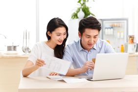 Young couple sitting in their kitchen and looking at financial documents a laptop