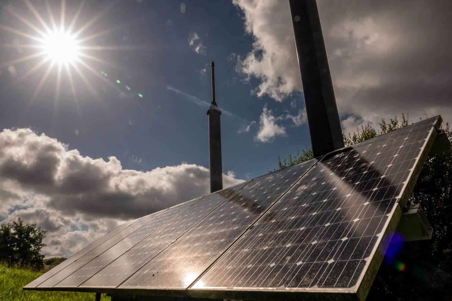 The sun shines on solar panels with grassland behind it.