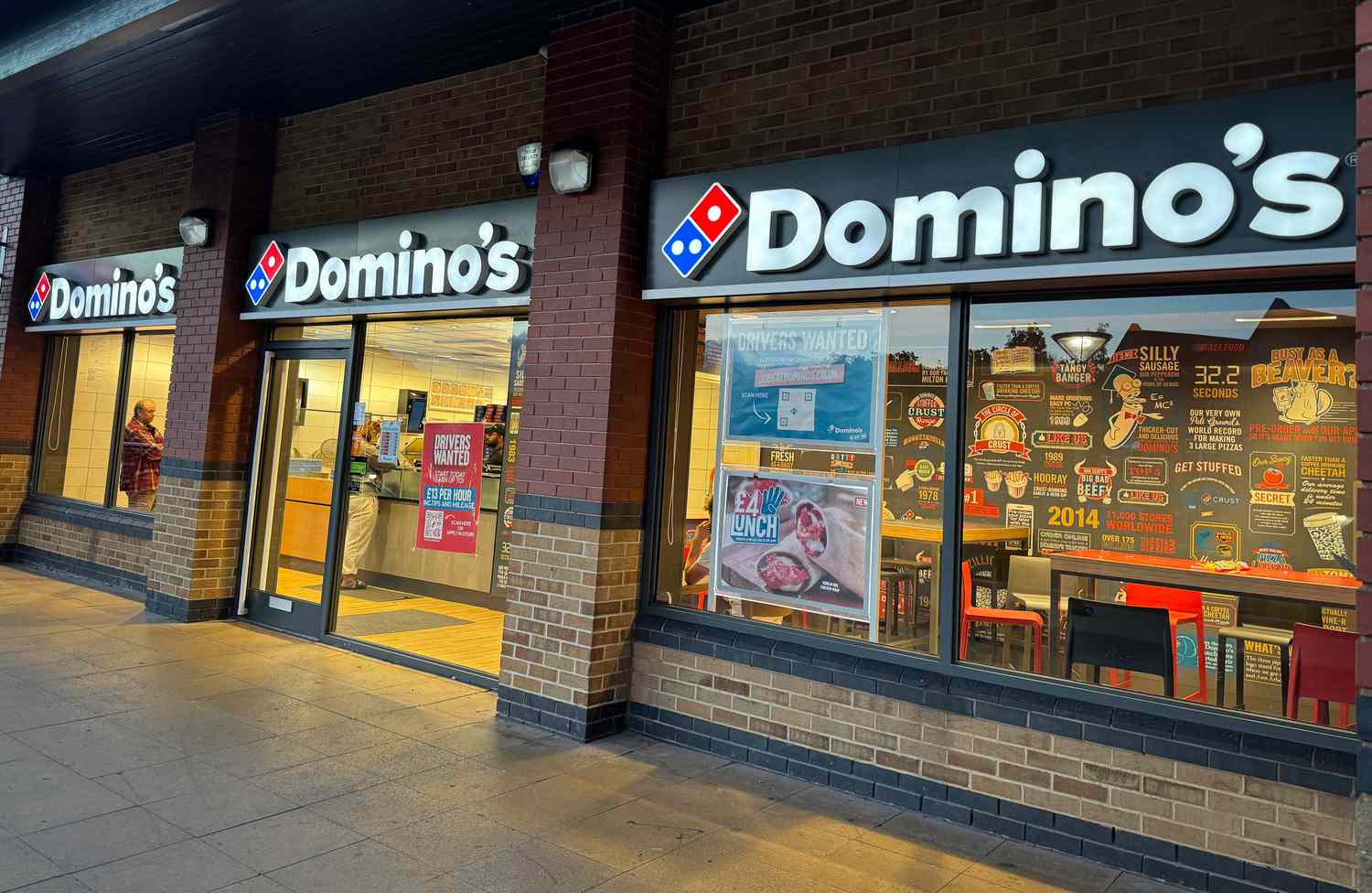 The Domino's Pizza logo is seen above the windows and doors of a restaurant.