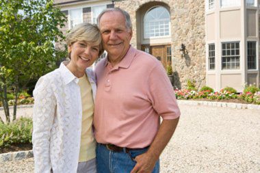 Older couple standing in front of home 