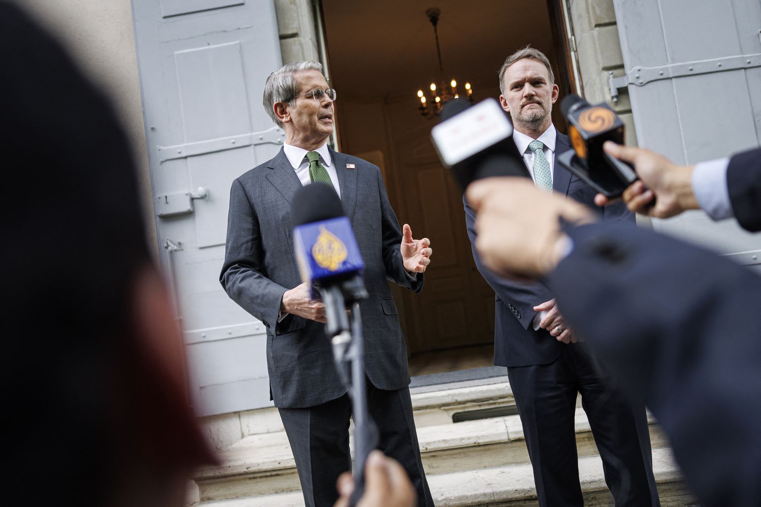 Scott Bessent and Jamieson Greer stand in front of the doorway at the residence of the permanent Swiss ambassador to the United Nations. Microphones are pointed toward them as they address reporters.