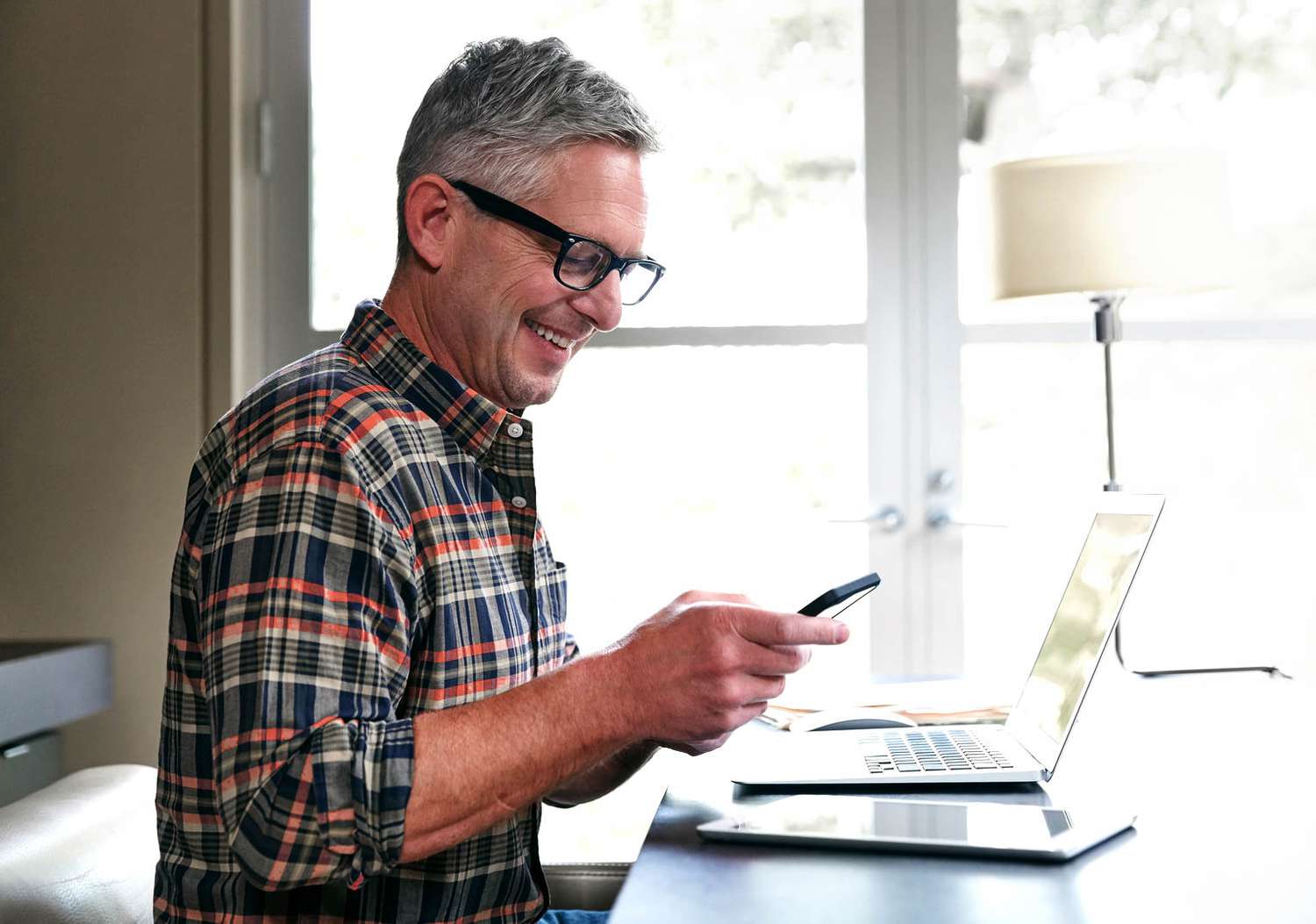 Man working on a laptop looking at his cell phone