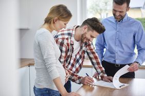 Couple With Real Estate Agent Signing Contract in Kitchen of New Apartment