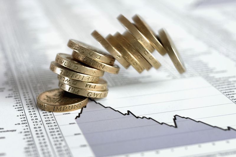 A stack of British pound coins falling on list of share prices.