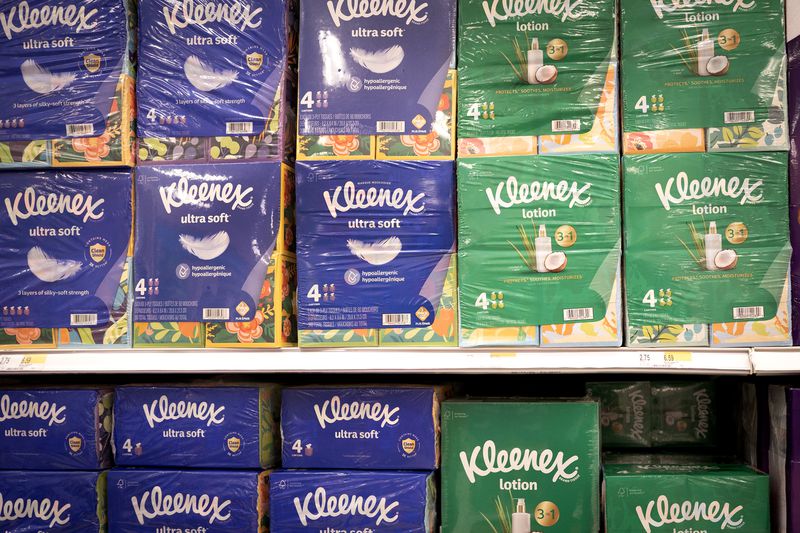 Purple and green boxes of Kleenex are stacked on top of each other in a store.