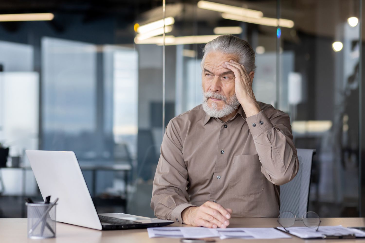 Man sitting at a desk looking at a laptop seeming worried.