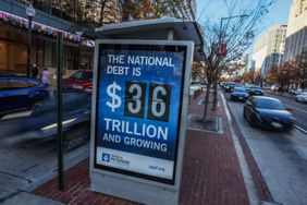 A street advertisement showing the U.S. national debt as $36 trillion, placed at a busy urban sidewalk corner with cars passing by