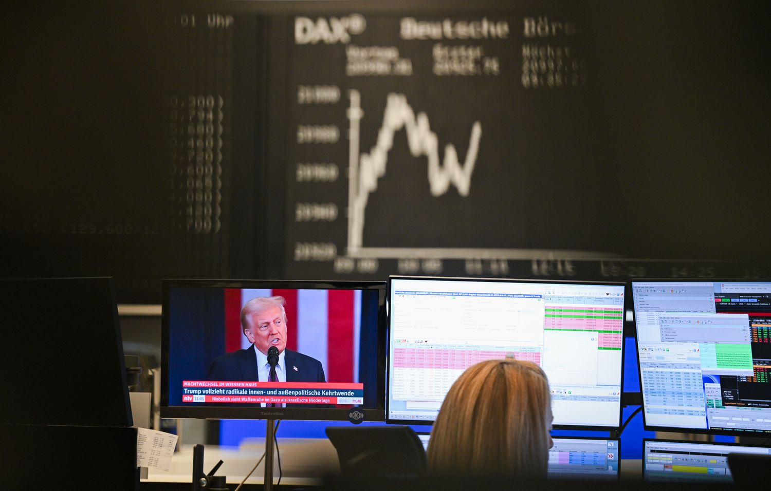 The Dax curve shows upward and downward movements in the trading hall of the Frankfurt Stock Exchange, while the new US President Donald Trump can be seen on a screen.