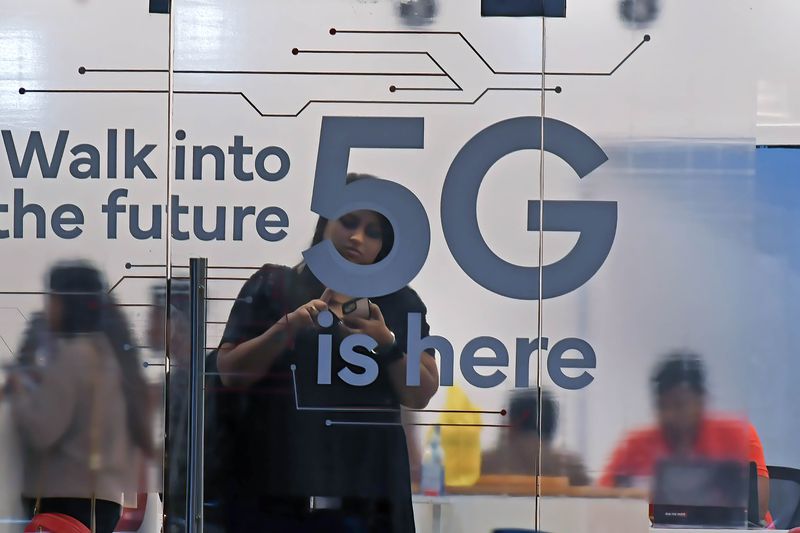 A person checks their mobile phone inside a mobile service provider store advertising 5G service.