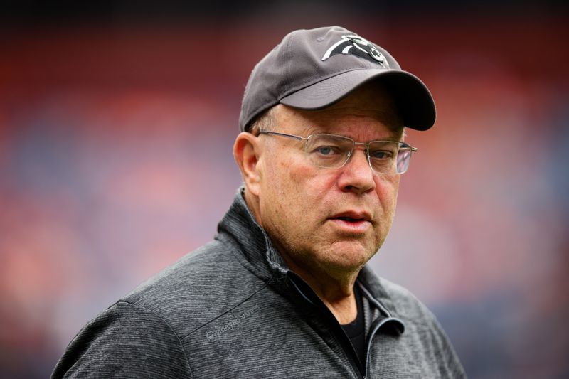 A man is seen wearing glasses, a gray sweatshirt, and a dark gray hat with a Carolina Panthers logo on it.