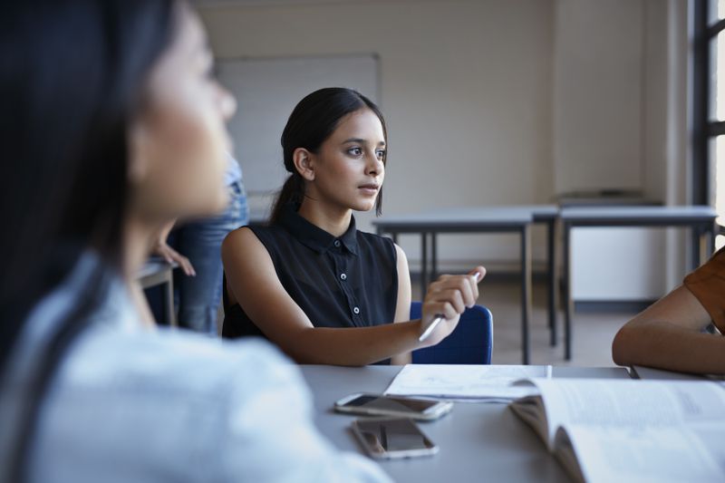Student sits at desk with others holding a pen