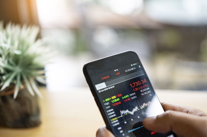 Hands holding a smartphone with stock trading information on the screen
