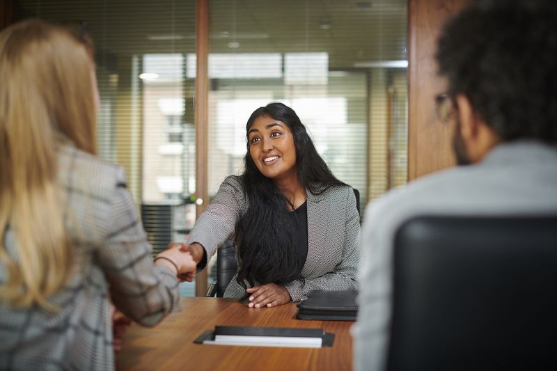 A job hunter shaking hands with someone over a conference room table. 