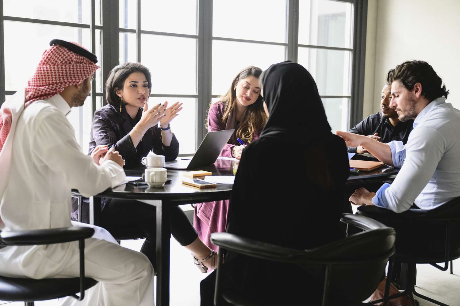 People in a business meeting, sitting around the table while drinking coffee and evaluating specific risks of oil sector being presented. 