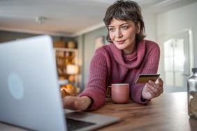 A woman sits at the kitchen counter and researches for information about the best bitcoin debit cards.