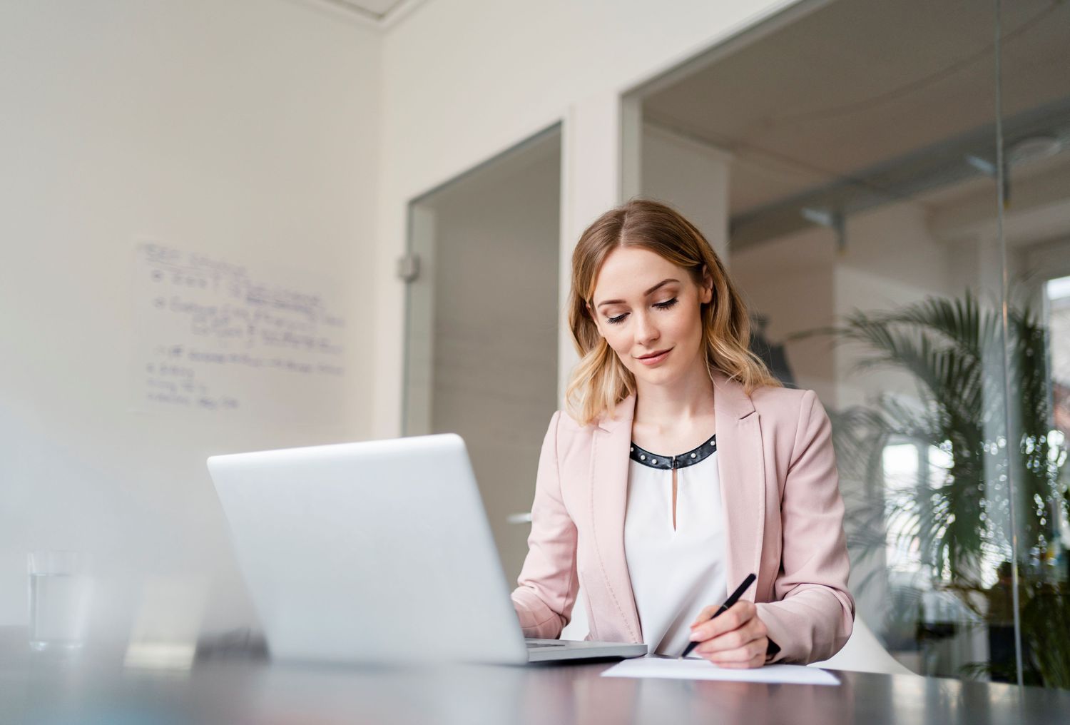 A woman takes notes and works on a computer.
