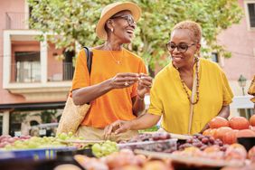 Two mature women shopping at an outdoor food market. 