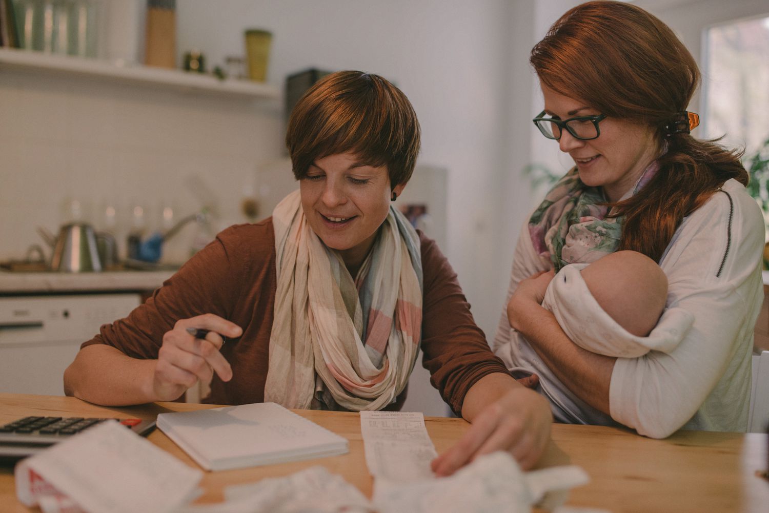 A couple does their household budget at home while one holds a newborn child.