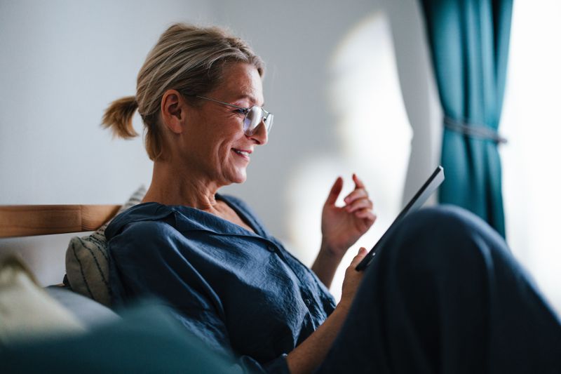 Older woman sitting at home and looking happily at her finances online