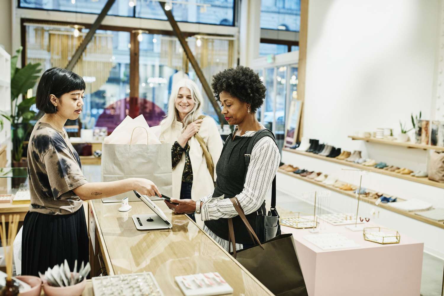 One Woman Paying Another Working as a Retail Salesperson as a Third Woman Looks on in a Retail Shoe Store.