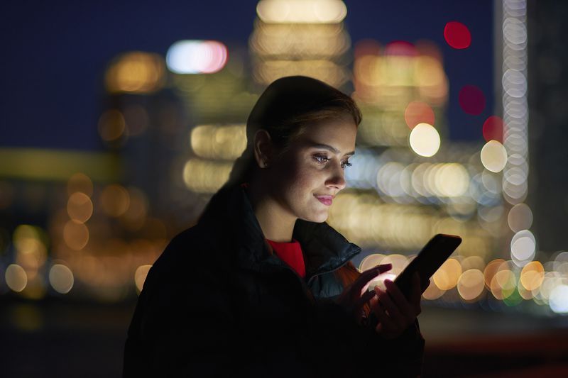 a woman checking her phone with a cityscape background at night