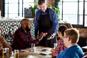 African American Man making contactless card payment on machine for lunch with colleagues