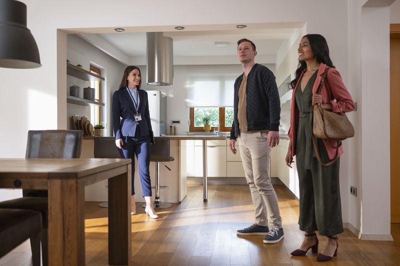 Three people in a modern kitchen, one appearing to be a real estate agent and two others appearing interested in the property