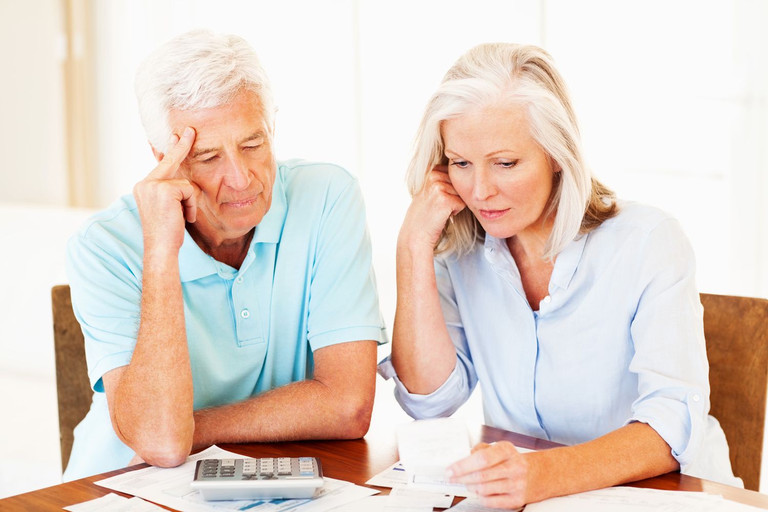 Older couple sitting at their kitchen table and looking with concern at mortgage documents and a calculator