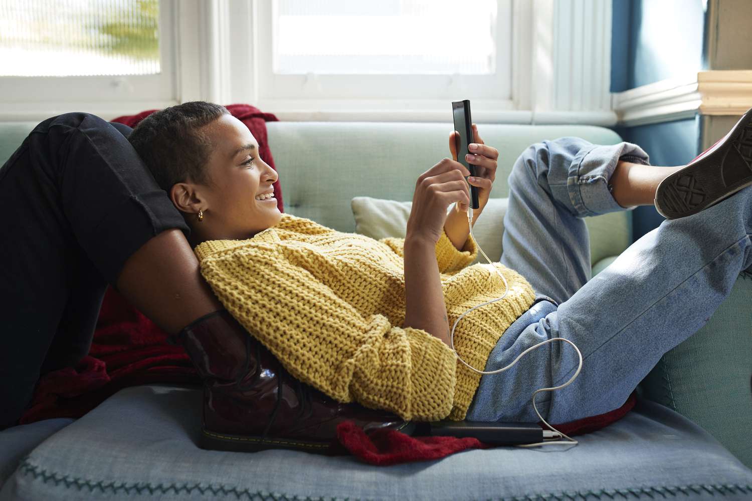 A woman lounges on a couch with a cell phone.