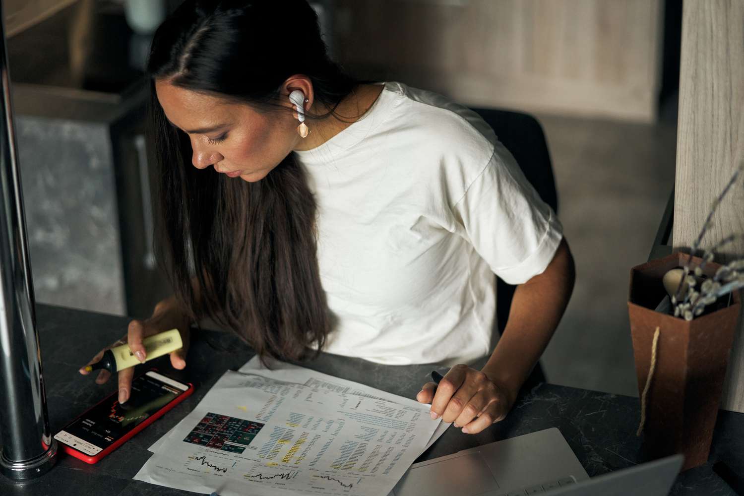 Woman doing paperwork and working at smartphone with wireless earphone at home.