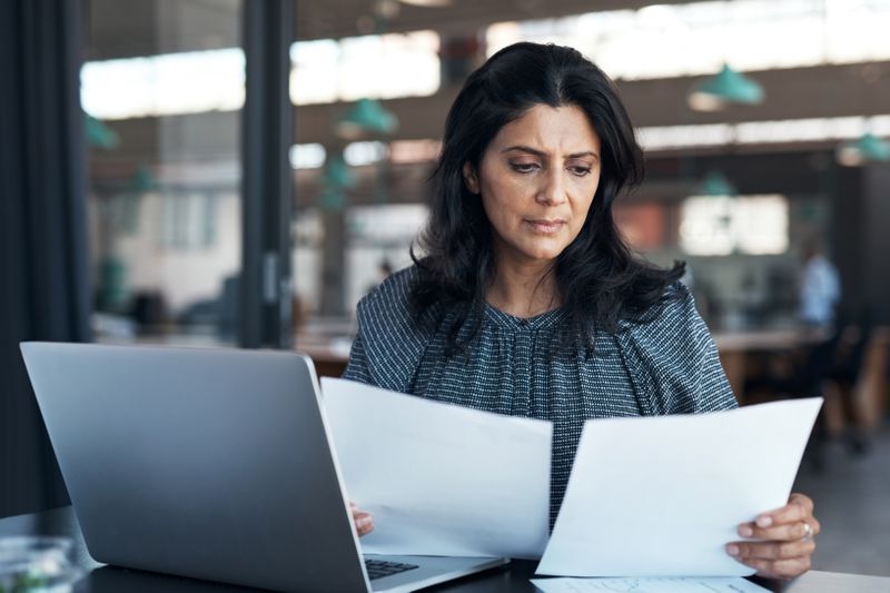 An investor sits at a desk with printed documents in their hands as they review the difference between investing in a Roth IRA account and a Traditional IRA account.