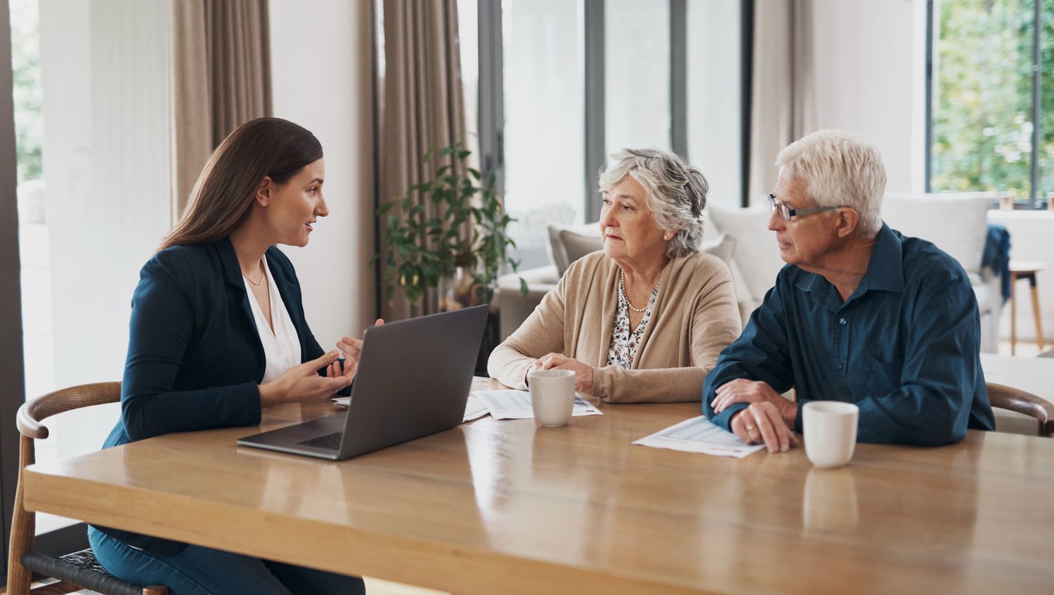 A woman conversing with an elderly couple at a table with a laptop