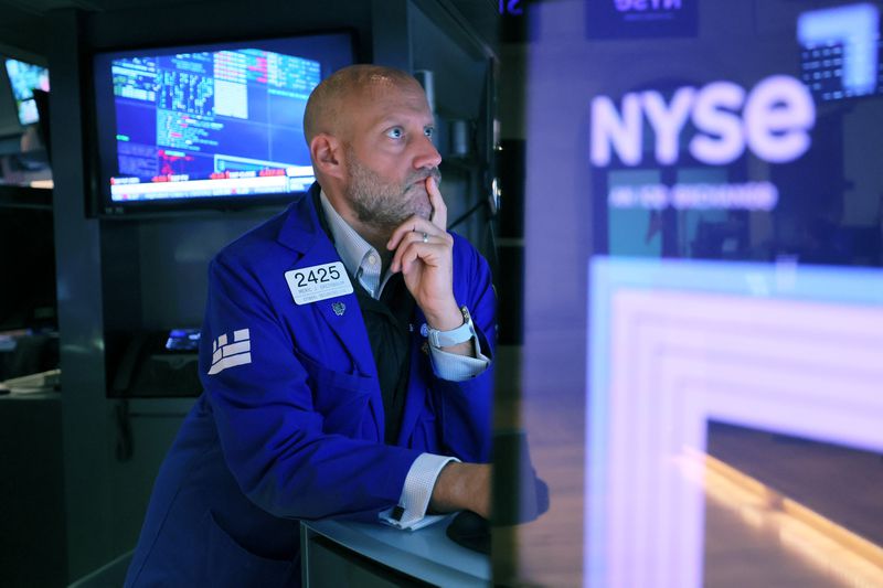 A trader in a blue jacket leans on a desk while looking at a computer screen on the floor of the New York Stock Exchange.
