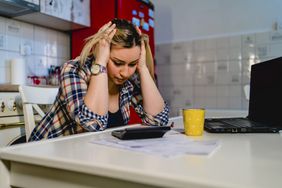 Upset woman sitting in the kitchen worrying over student loan payment.