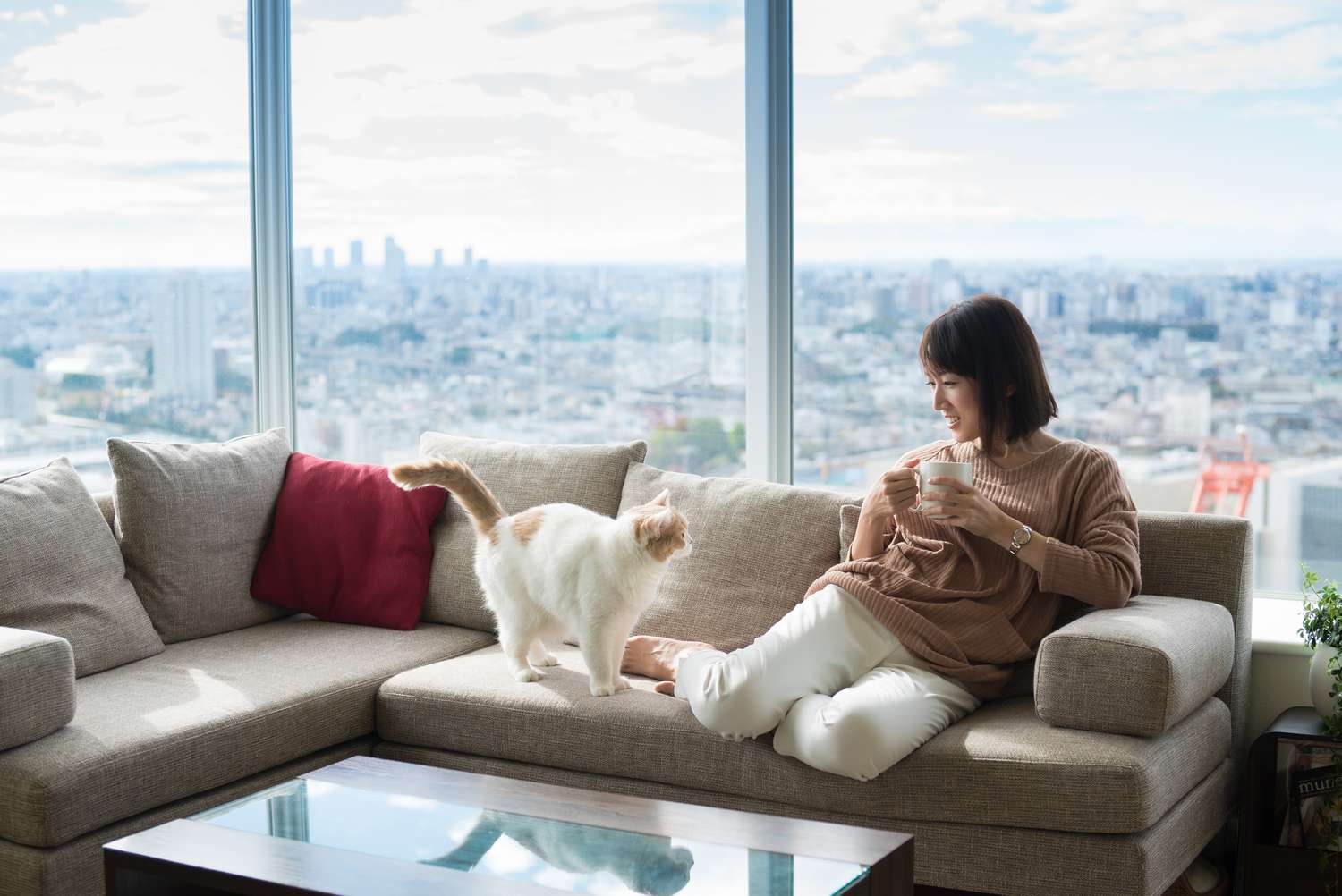 Woman on a couch with a cat holding a coffee cup in a high rise condo