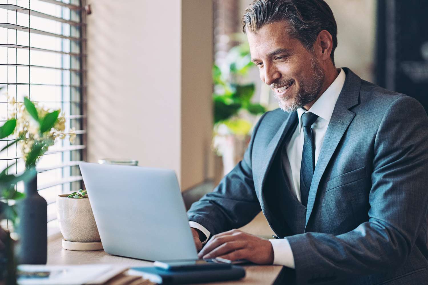 Middle aged man in a business suit smiling while working on a laptop.