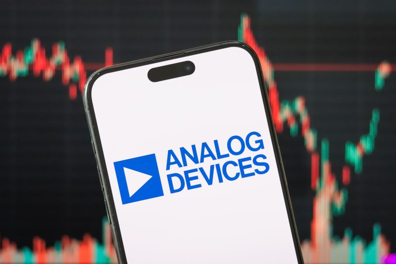 The blue Analog Devices logo is seen on a phone screen, with a stock chart in the background.