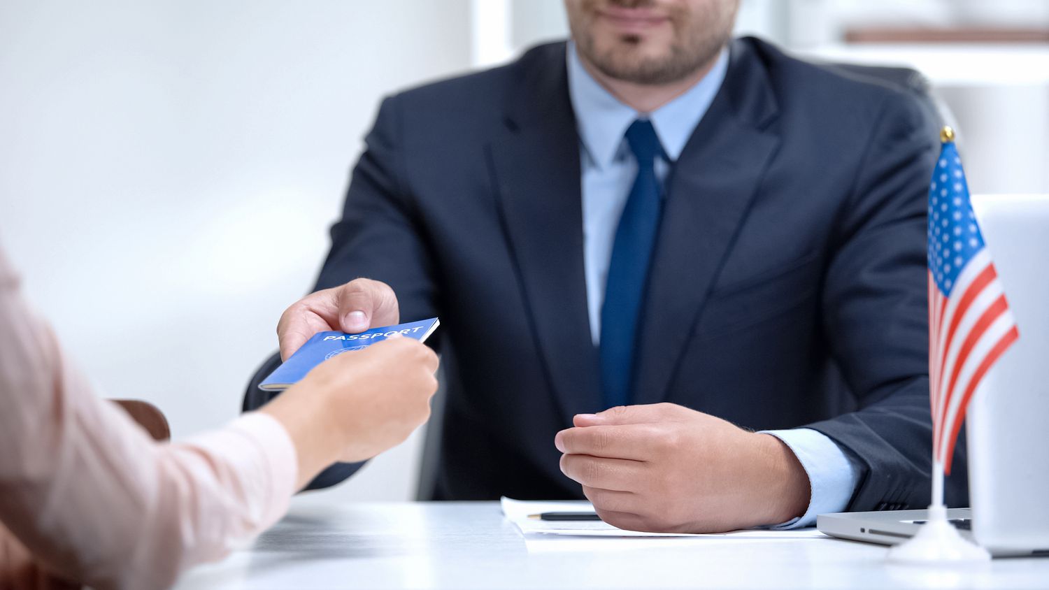 A man at a desk handing a passport to a woman in a close up of their hands. 