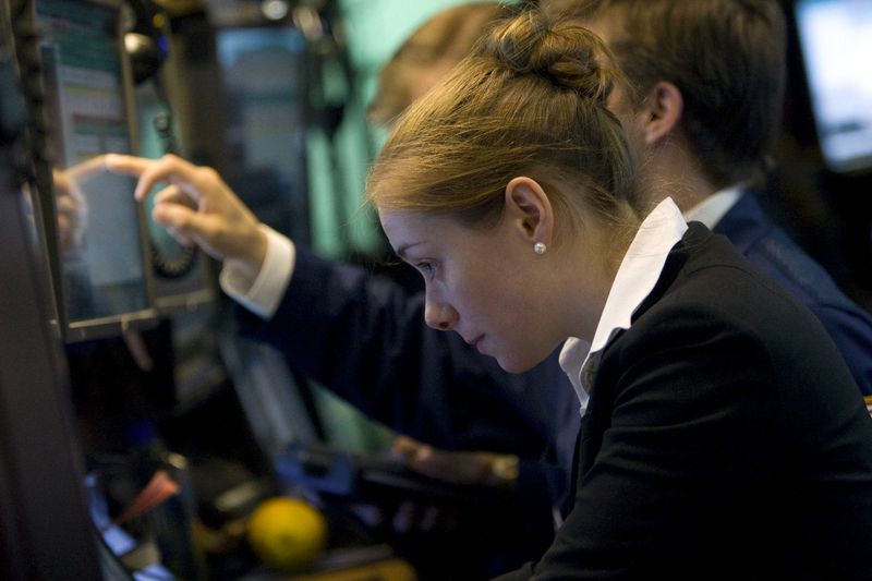 A female trader is pointing to a screen while looking down.