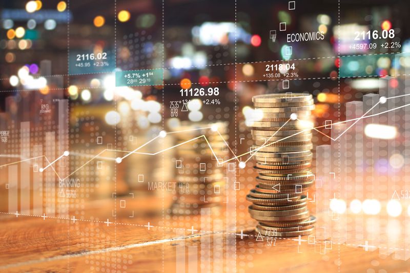 A double exposure with business charts, a stack of coins and a night city background.