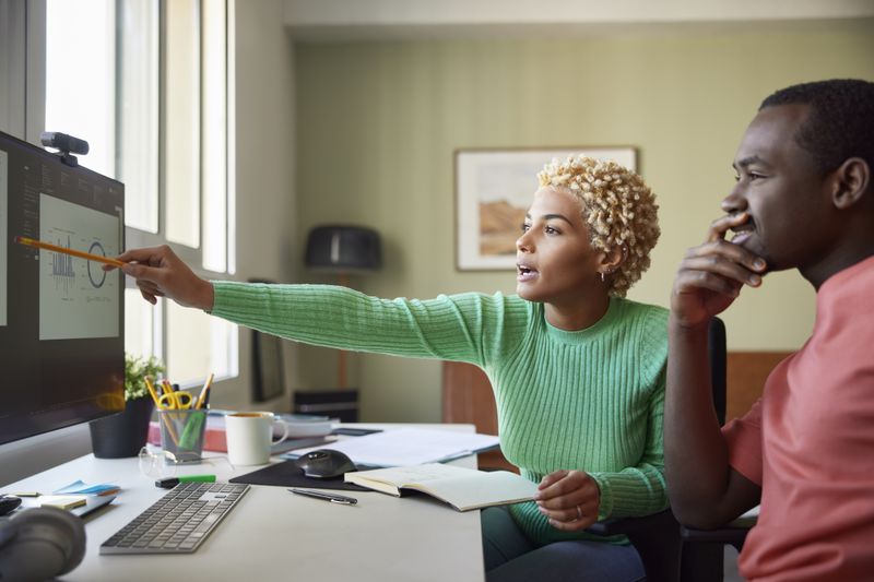 Woman sitting by a man points to graphs on a monitor
